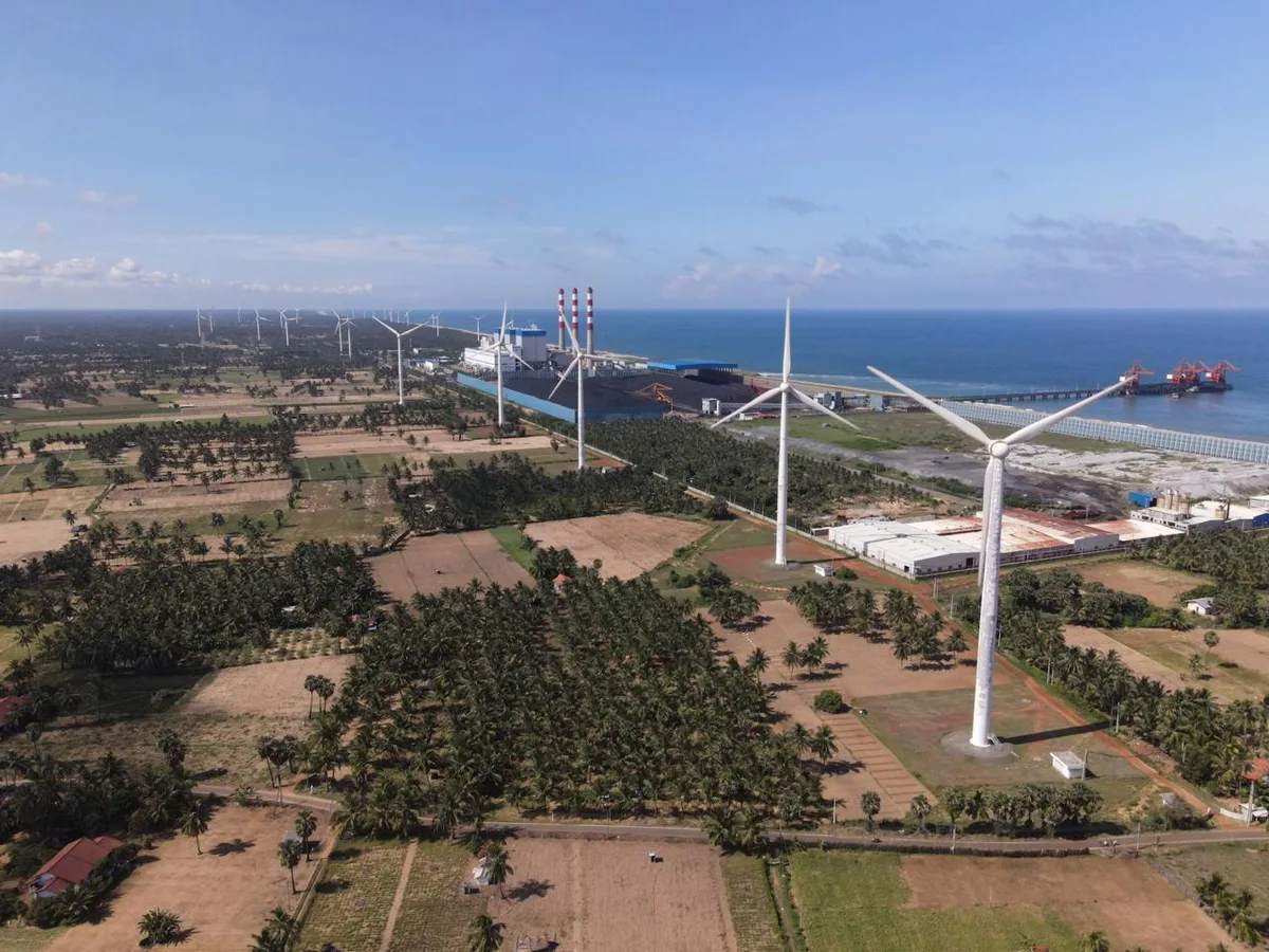 Aerial site-context photograph showing coastal wind turbines, palms and existing generation infrastructure.